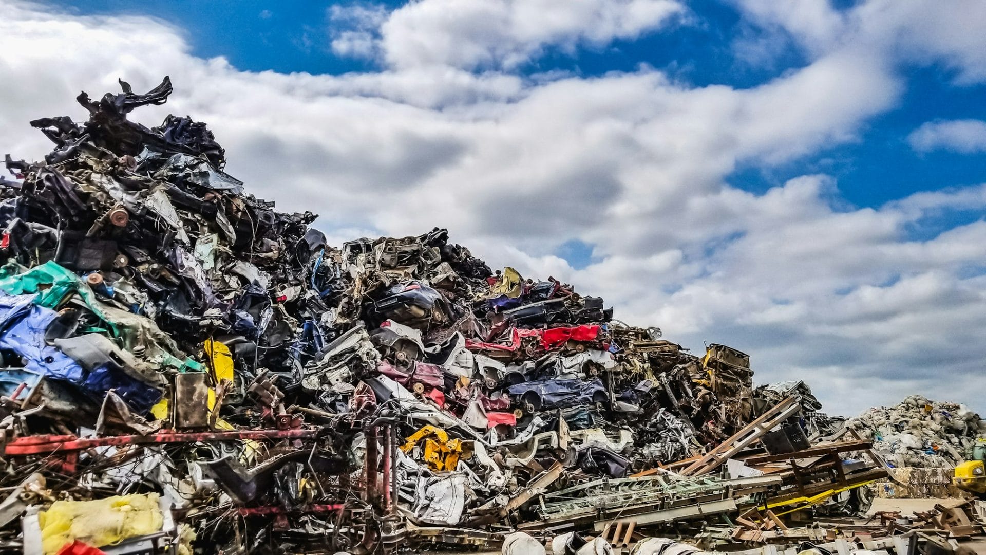 Crushed vehicles at a scrap yard against blue cloudy sky